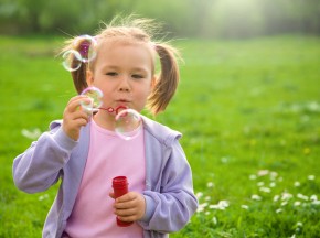 Little girl blows soap bubbles on meadow